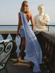Woman in a blue dress standing next to a classical statue by a waterfront.