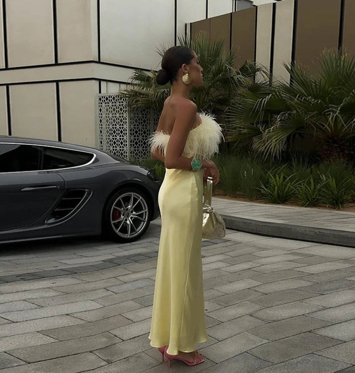Woman in a yellow dress standing next to a car with a modern building and plants in the background
