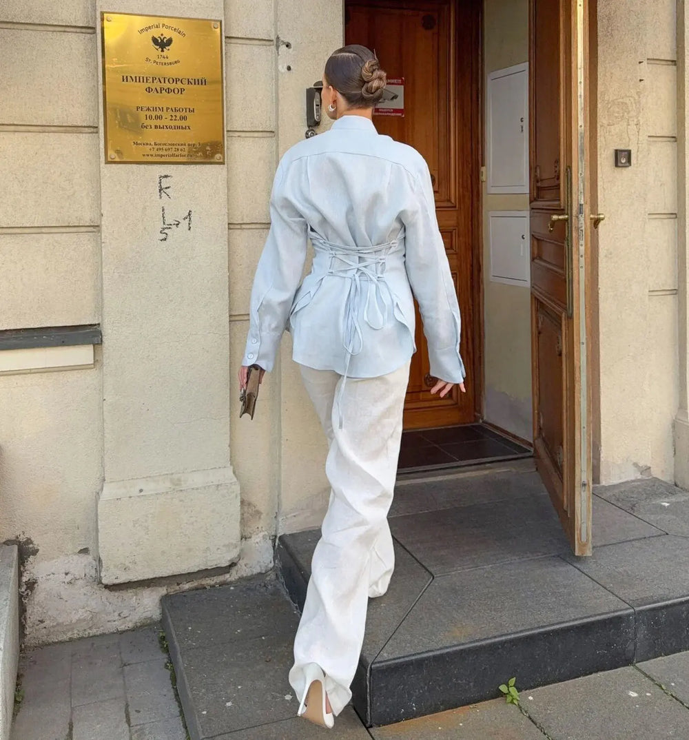 Person in light blue shirt and white pants exiting a building with a sign on the wall.