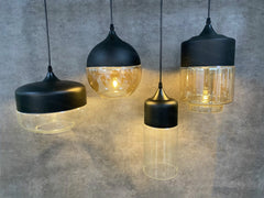 Four pendant lights with black and gold finishes on a gray concrete background