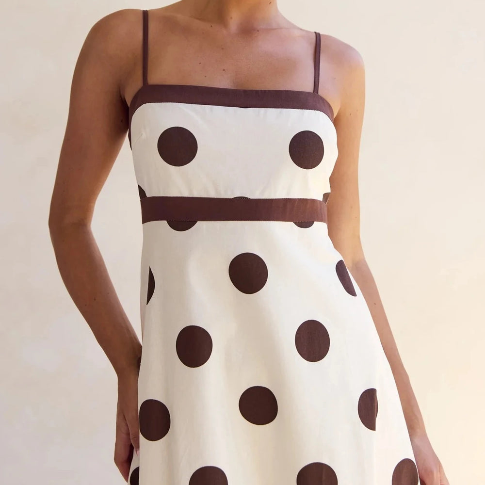 White dress with brown polka dots and a brown belt on a plain background