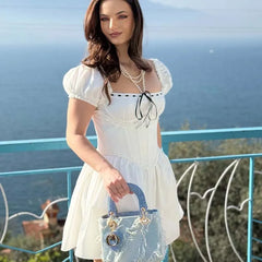 Woman in a white dress holding a clear handbag with a scenic background