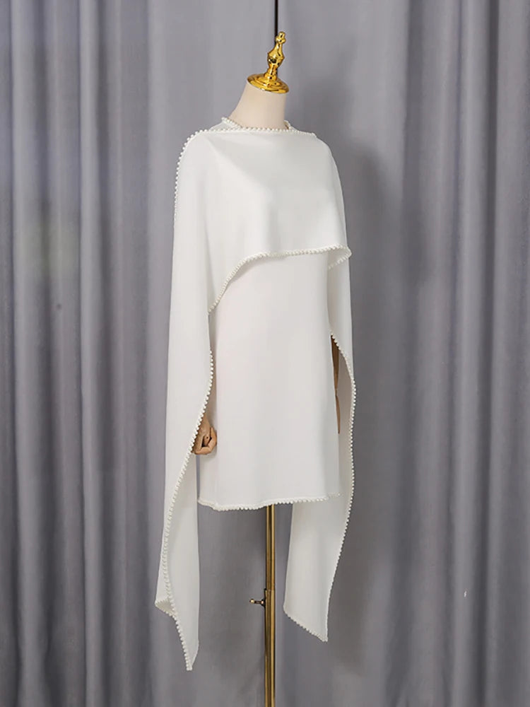 White poncho on a mannequin against a gray curtain background