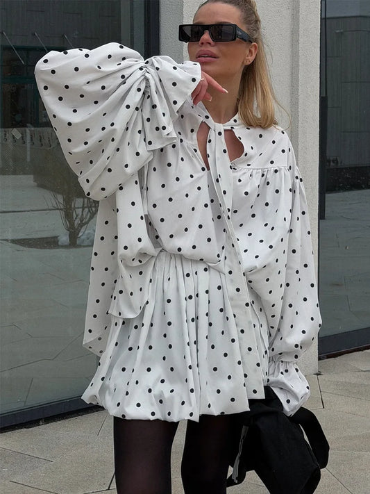 Woman wearing a white polka dot dress with large bow sleeves outdoors.