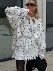 Woman wearing a white polka dot dress with large bow sleeves outdoors.