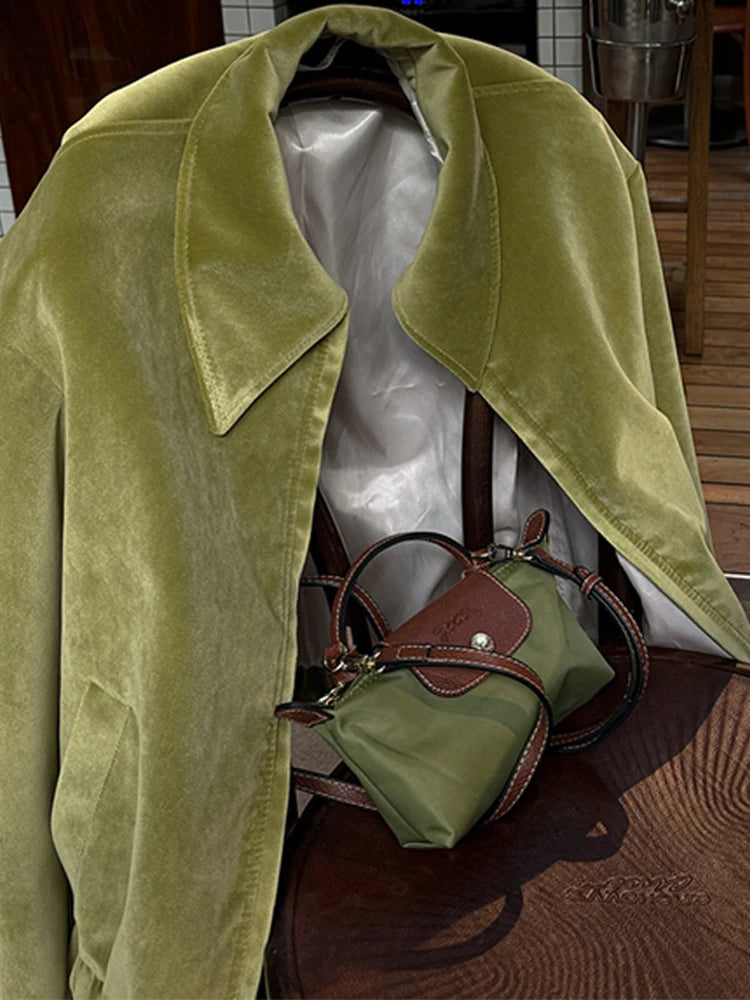 Green velvet coat draped over a mannequin with a matching handbag on a wooden floor.