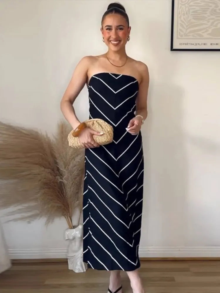 Woman wearing a strapless navy dress with white stripes, holding a woven bag indoors.