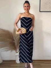 Woman wearing a strapless navy dress with white stripes, holding a woven bag indoors.