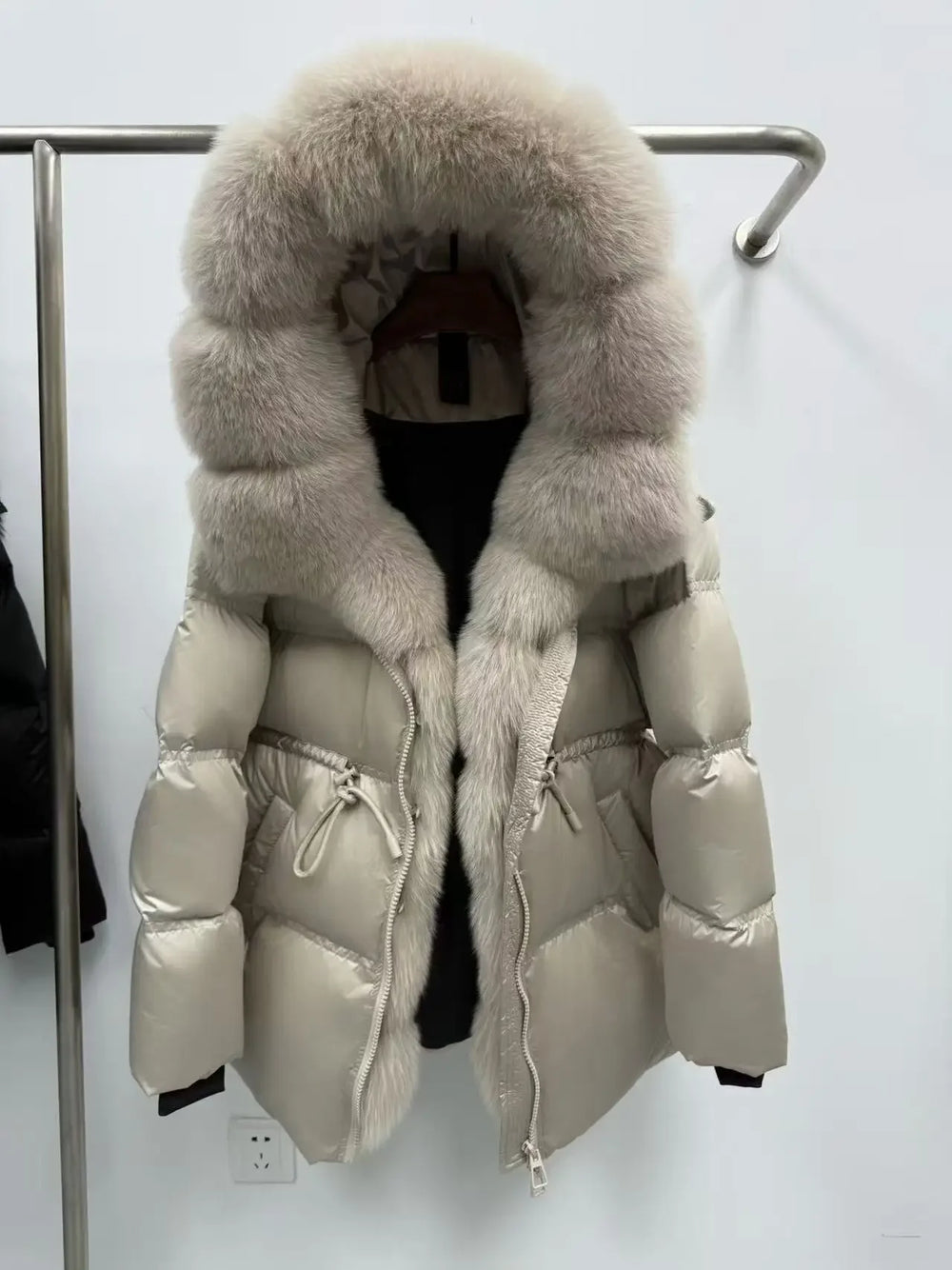 Beige puffer jacket with large fur hood on a rack against a white background