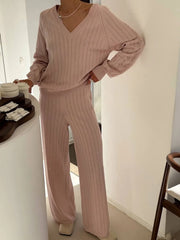 Person wearing a pink ribbed sweater and pants in a kitchen setting.