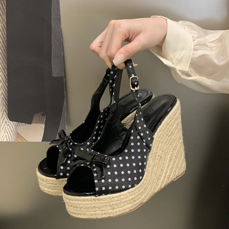 Black polka dot wedge sandals with espadrille sole held by a hand against a neutral background