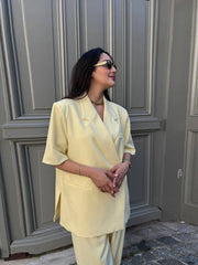 Woman in a light yellow outfit standing in front of a gray door.