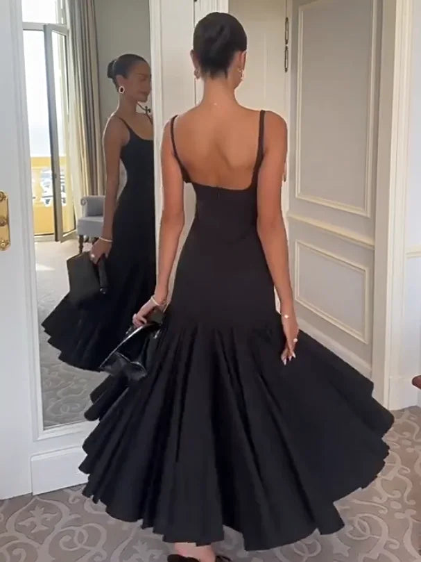 Woman in a black evening gown standing in a room with a mirror reflection.