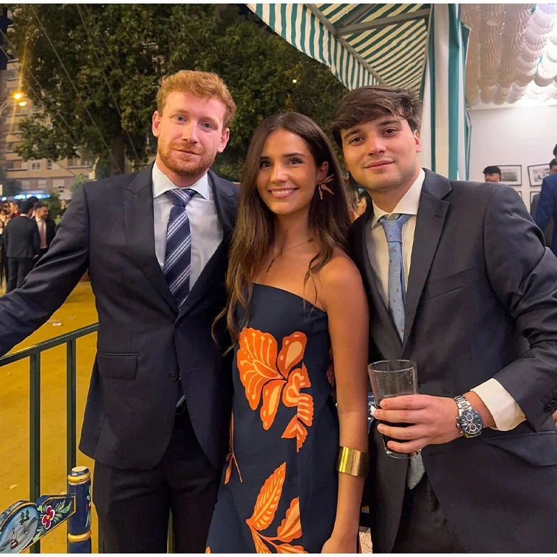 Three people posing together outdoors, two in suits and one in a floral dress.