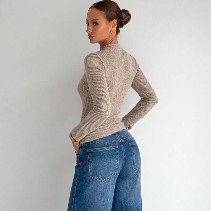 Woman wearing a beige sweater and blue jeans against a plain background