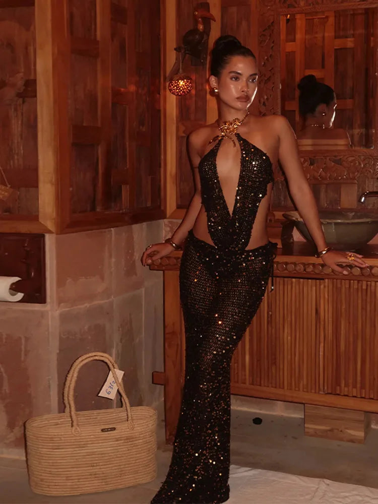 Woman in a black sequin dress standing in a spa-like setting with a woven bag.