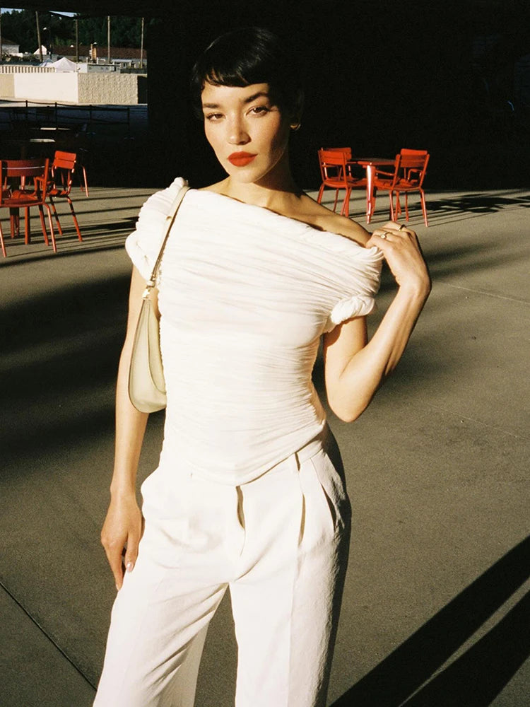 Model in a white ruched off-shoulder top and white trousers.