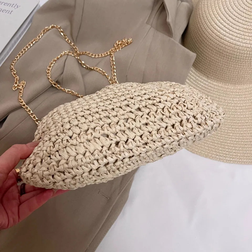 Beige woven handbag with gold chain held by a hand, with a neutral background.
