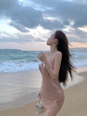 Woman in a beige dress standing on a beach with ocean and cloudy sky in the background