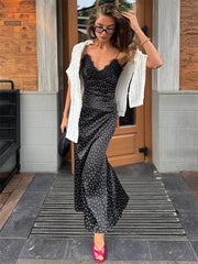 Woman in a black polka dot dress with a white cardigan standing outside a building.