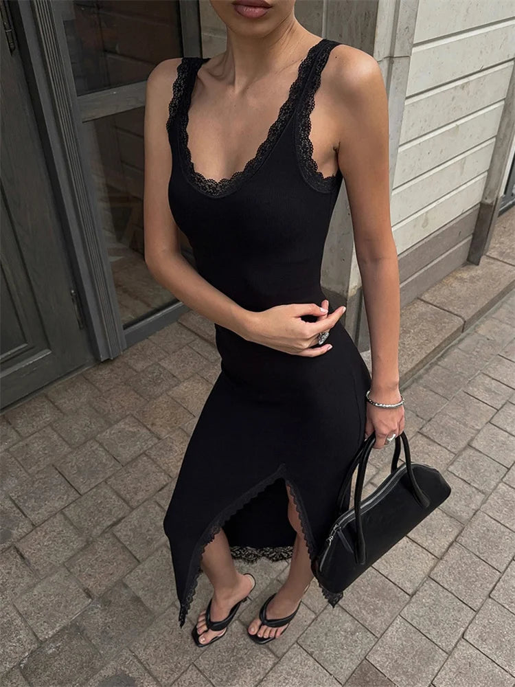 Woman wearing a black lace-trimmed dress holding a black handbag on a sidewalk.