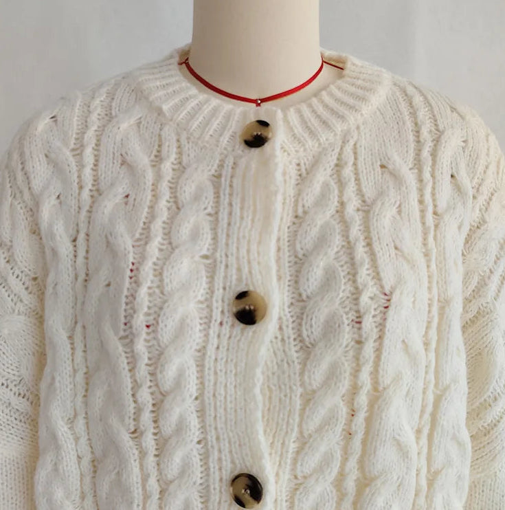 White cable knit cardigan on a mannequin with a plain background