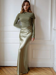 Woman wearing a green satin gown standing against a white wall.