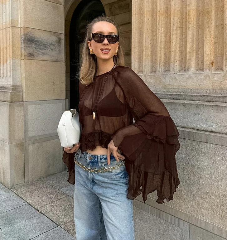 Woman in a brown layered top and blue jeans standing in front of a stone building.