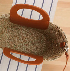 Woven handbag with orange handle on a striped fabric background