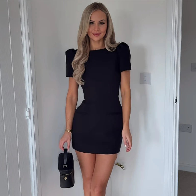 Woman wearing a black dress holding a matching handbag indoors.
