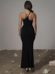 Woman wearing a black halter neck dress standing on a sandy surface with rocks.