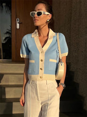 Woman wearing a light blue and white outfit with sunglasses and a handbag, standing outdoors.