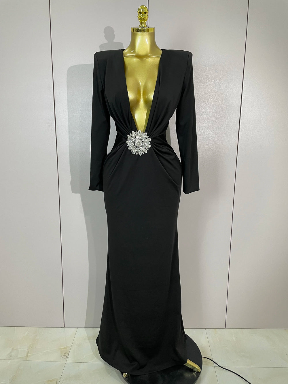 Black evening gown with a large brooch on a mannequin against a white background