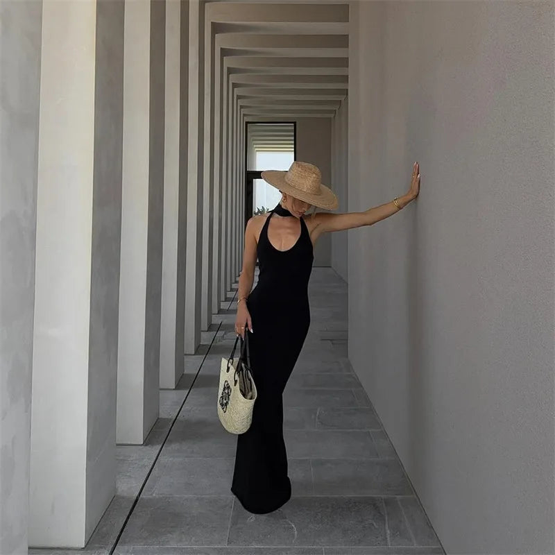 Woman in a black dress and straw hat standing in a long, narrow hallway.