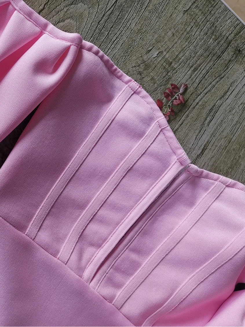 Close-up of a pink garment with pleated details on a wooden surface.