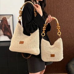 Person holding two beige woven handbags with wooden handles.
