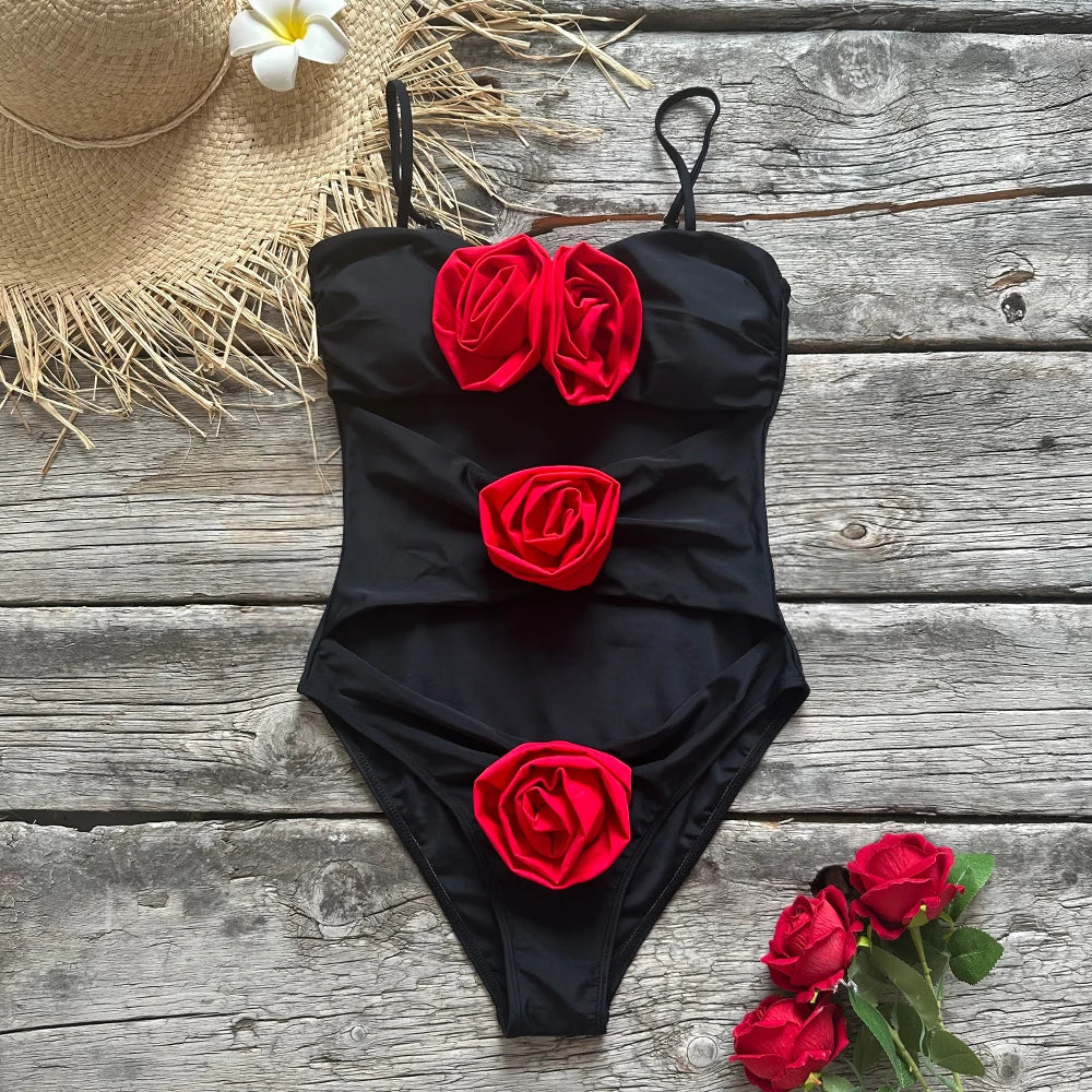 A black one-piece swimsuit with red rose embellishments laid flat on a rustic wooden surface, accompanied by a straw hat and flowers.