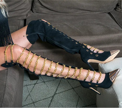 Person wearing black high-heeled shoes with gold chain details on a couch.