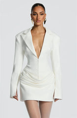 Woman wearing a white blazer dress with a plunging neckline on a plain background