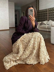 Person sitting on a couch with a textured blanket, taking a mirror selfie in a minimalistic room.