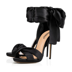 Black high-heeled sandals with large bow detail on a white background