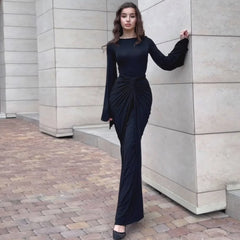 Woman in a black dress standing against a stone wall.