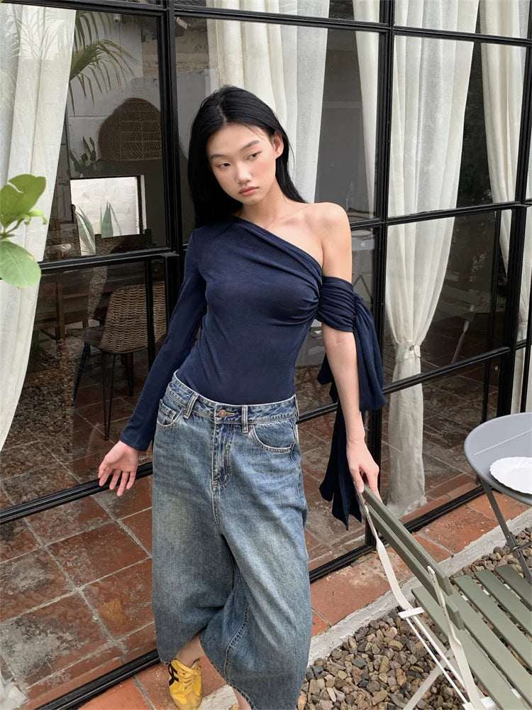 Woman wearing a navy top and blue jeans standing in front of a glass door.