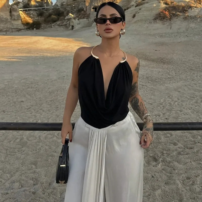 Woman in black top and white pants standing on a beach.