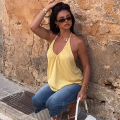 Woman in yellow top and blue jeans sitting against a stone wall.