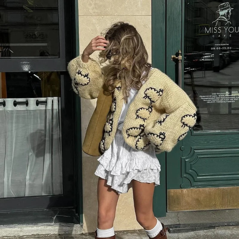 Woman wearing a patterned beige cardigan in front of a cafe entrance