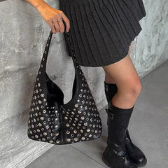 Person holding a black studded handbag with a gray textured wall background