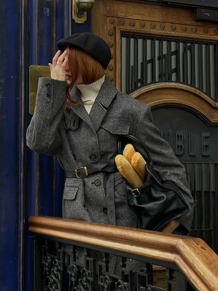 Person wearing a gray coat and black hat, holding a door handle, with a vintage-style building entrance in the background.