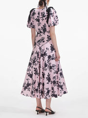 Pink dress with black floral pattern worn by a model on a white background