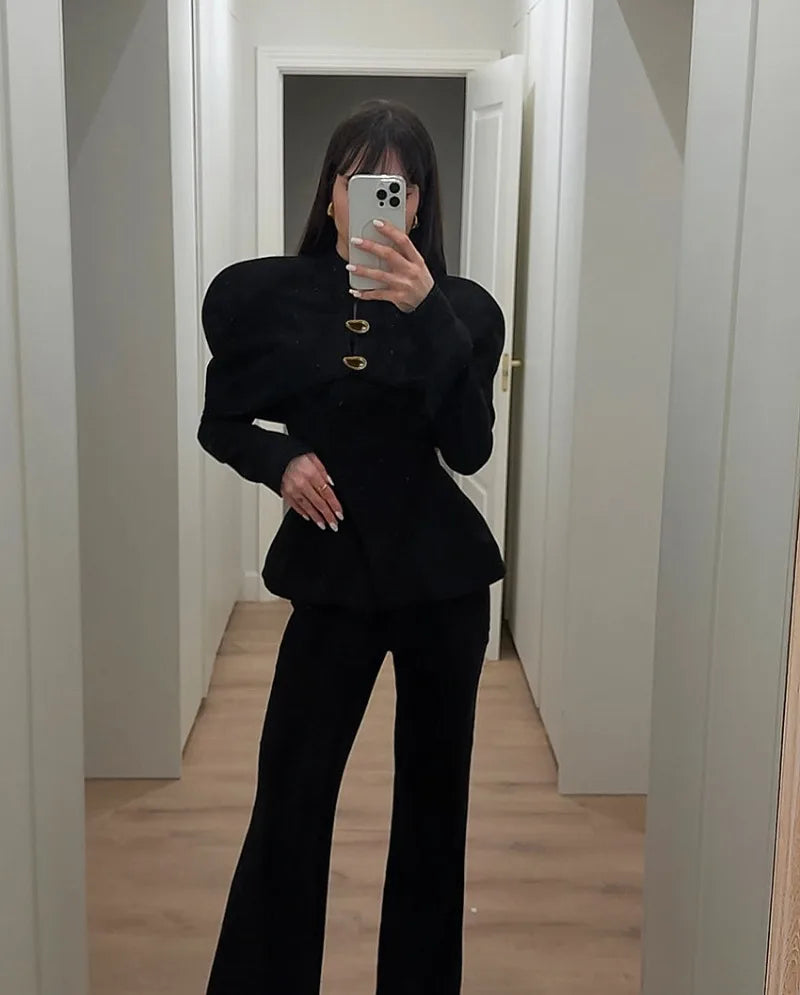 Person wearing a black outfit with a textured texture in a minimalistic room.